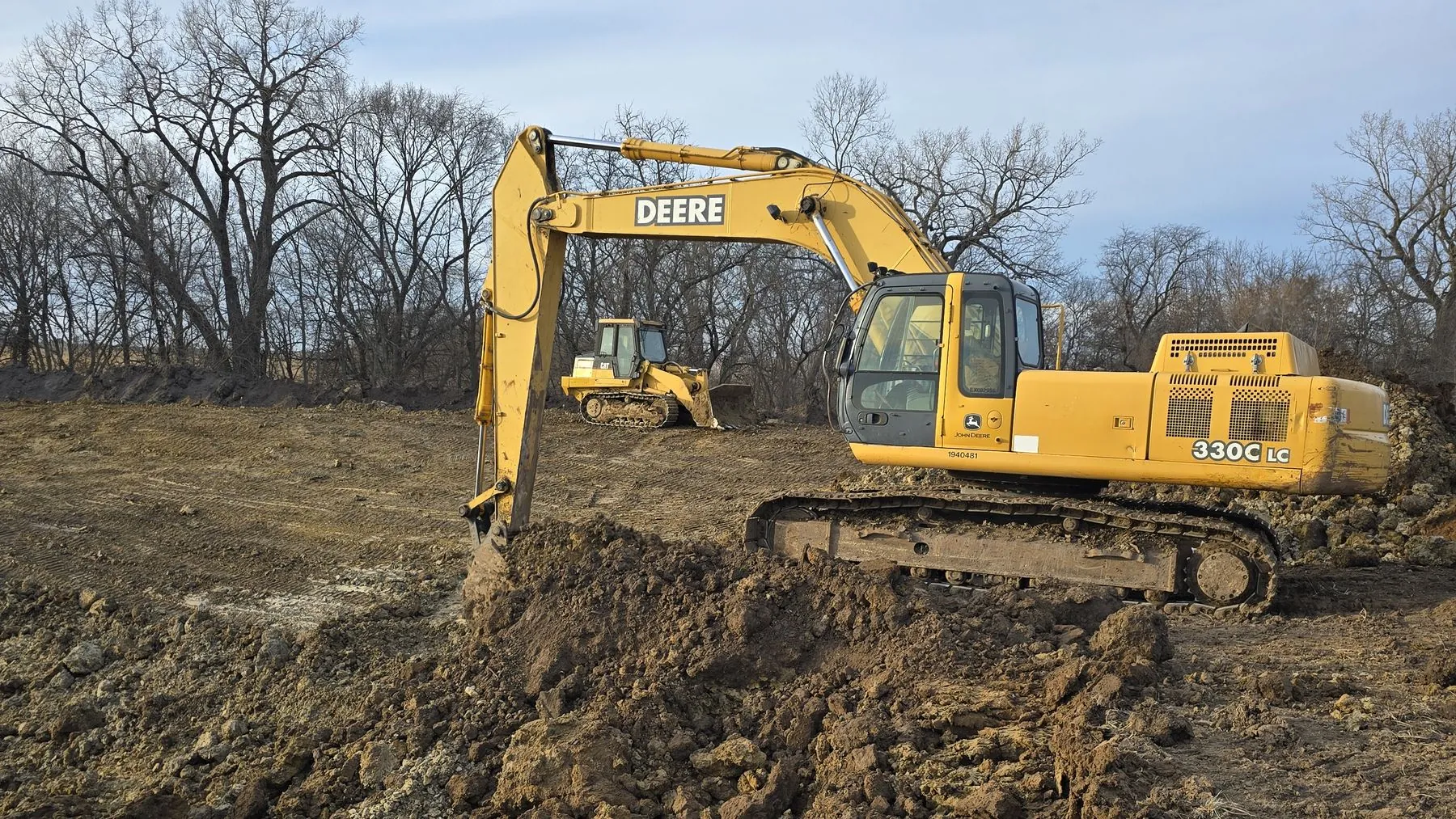 A tracked excavator working a cleared site under a wide sky