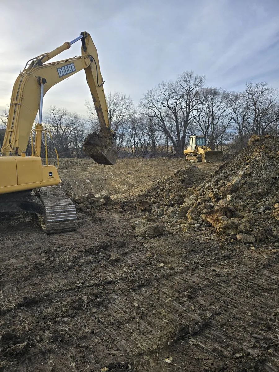 An excavator arm digging into fresh ground at the edge of a jobsite