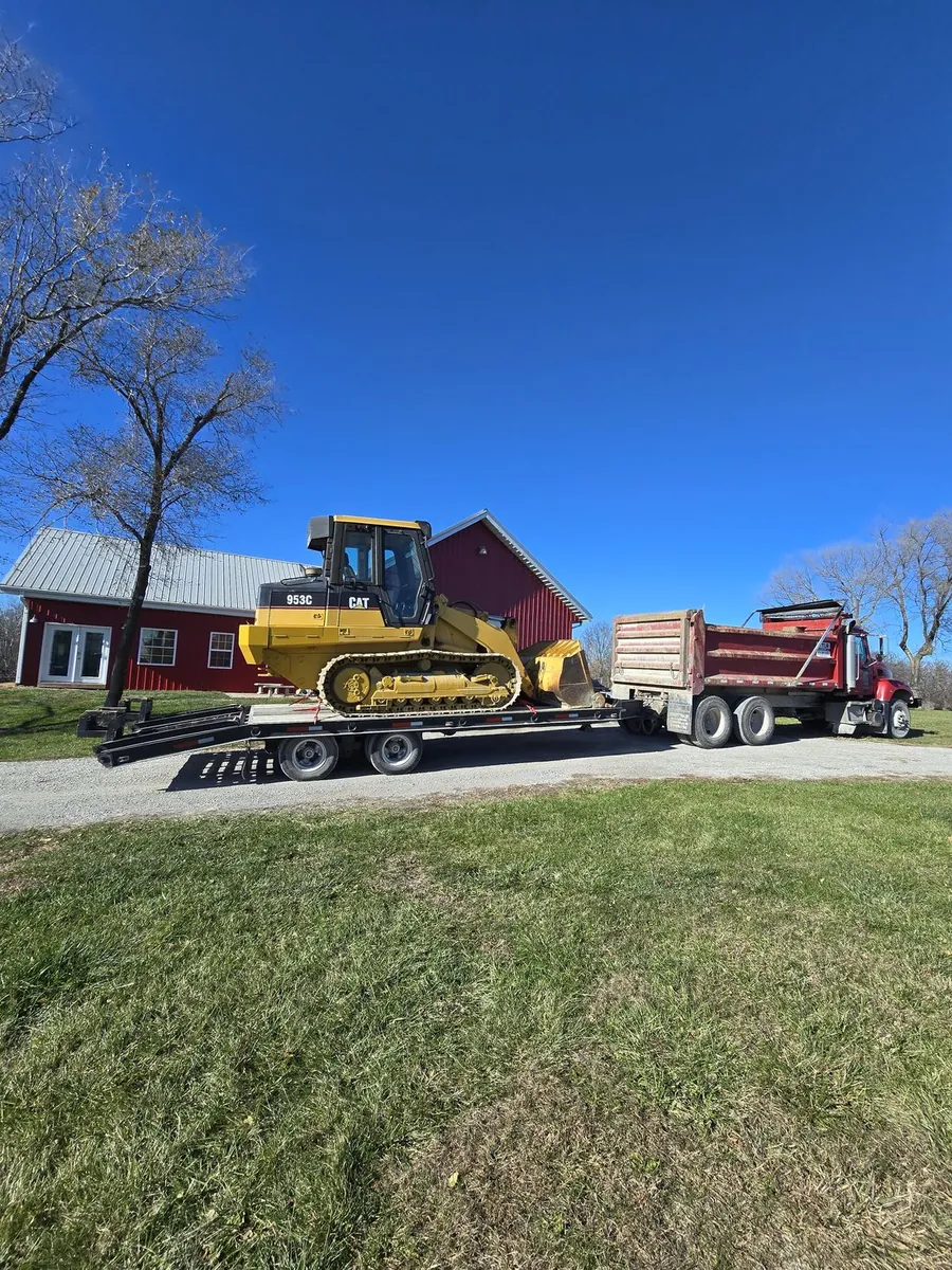 A track loader chained to a lowboy trailer next to a dump truck, ready to move to the next job